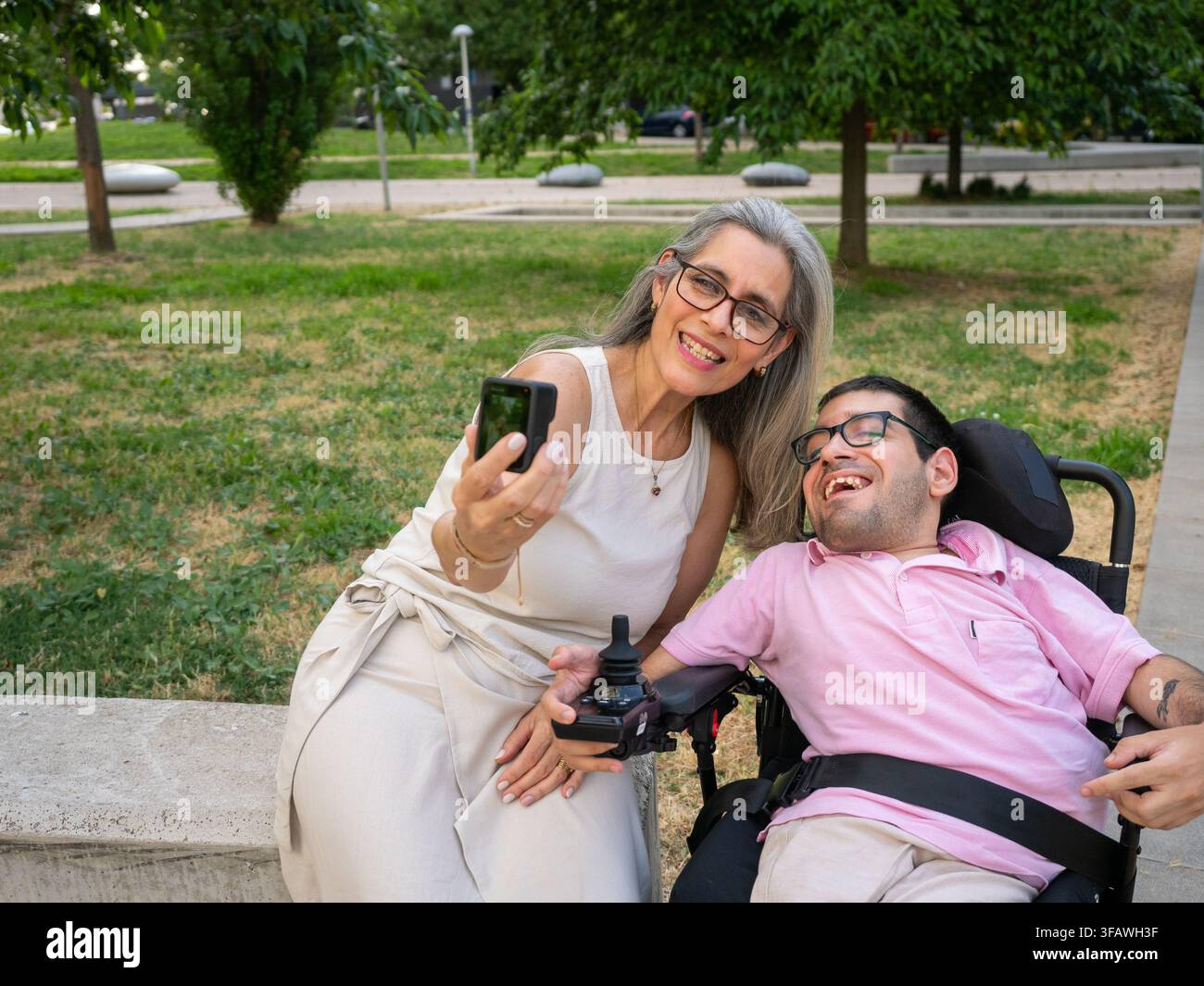 Madre e figlio adulto con disabilità che sorridono mentre scattano un selfie con una fotocamera d'azione Foto Stock