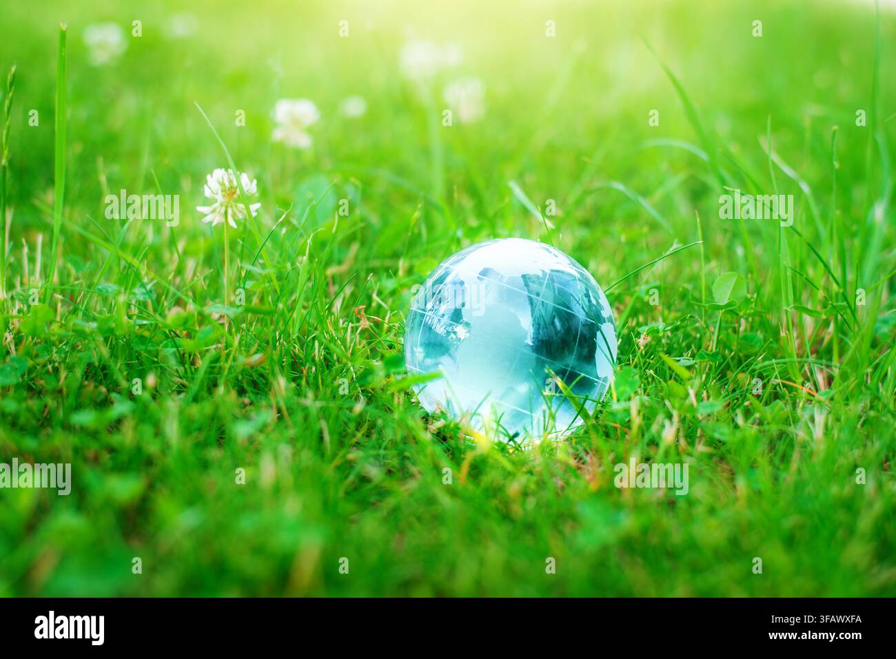 Sfera di cristallo di vetro sull'erba verde che riflette il cielo blu come un globo Foto Stock