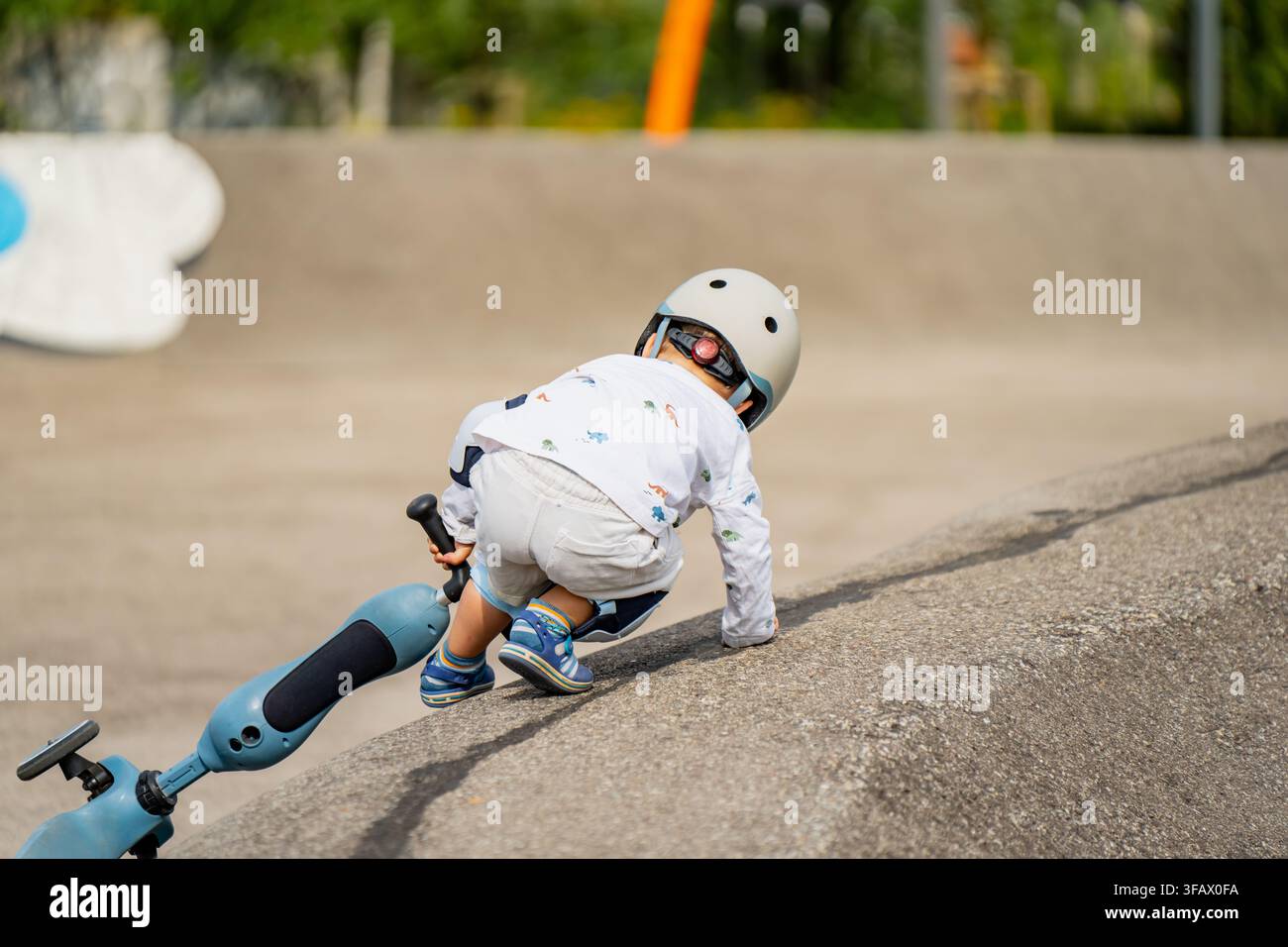 Bambino con casco di sicurezza che pratica l'equilibrio precoce e lo sviluppo motorio globale con uno scooter su superfici di rampa in cemento Foto Stock