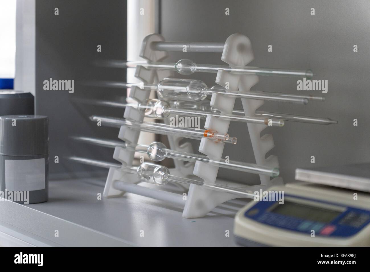 Pipette di vetro volumetriche appoggiate su un supporto di plastica bianca in un laboratorio di chimica con una bilancia digitale nelle vicinanze. Foto Stock