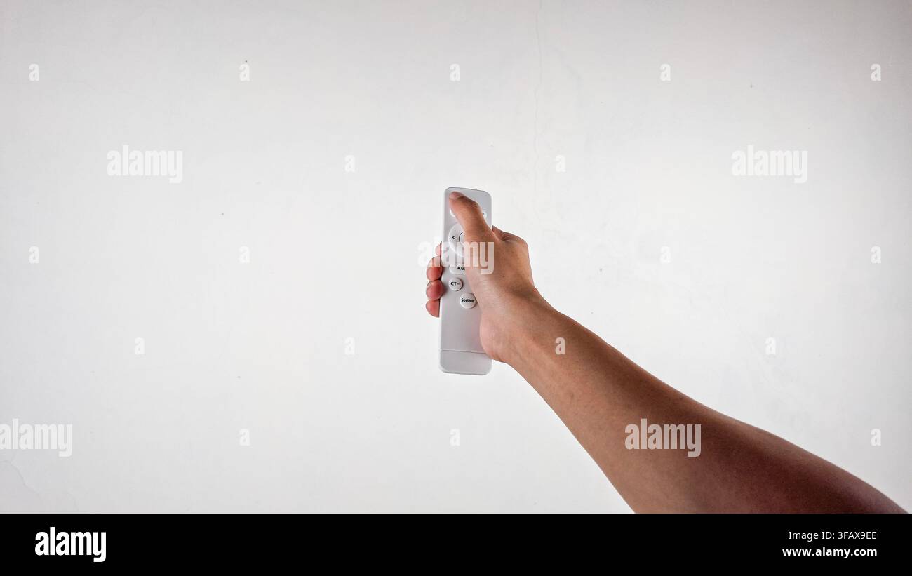 Mano che tiene un telecomando wireless bianco su sfondo chiaro Foto Stock