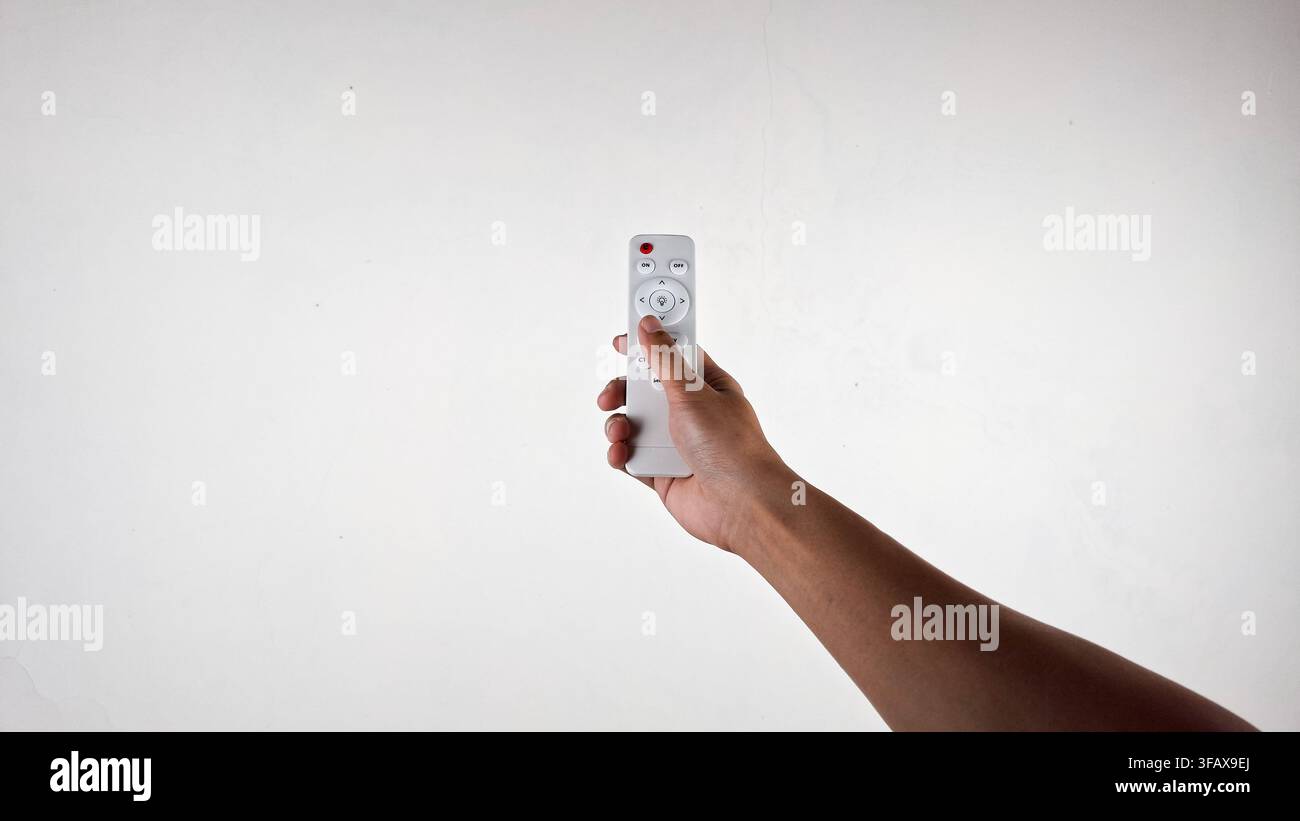 Mano che tiene un telecomando wireless bianco su sfondo chiaro Foto Stock
