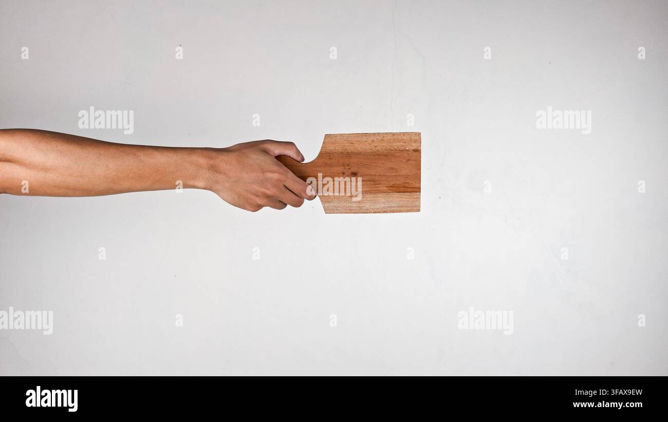 Mano che tiene un piccolo tagliere di legno con manico su sfondo bianco Foto Stock
