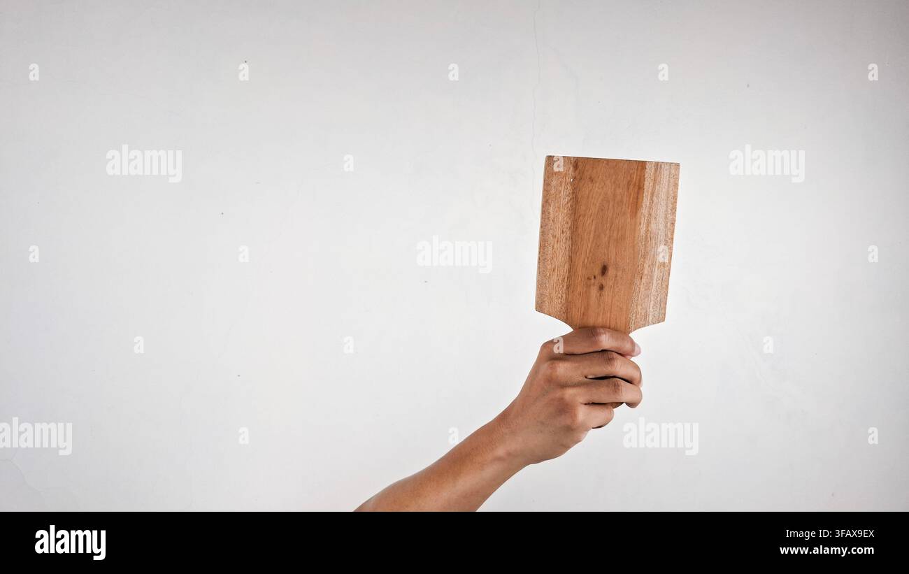 Mano che tiene un piccolo tagliere di legno con manico su sfondo bianco Foto Stock