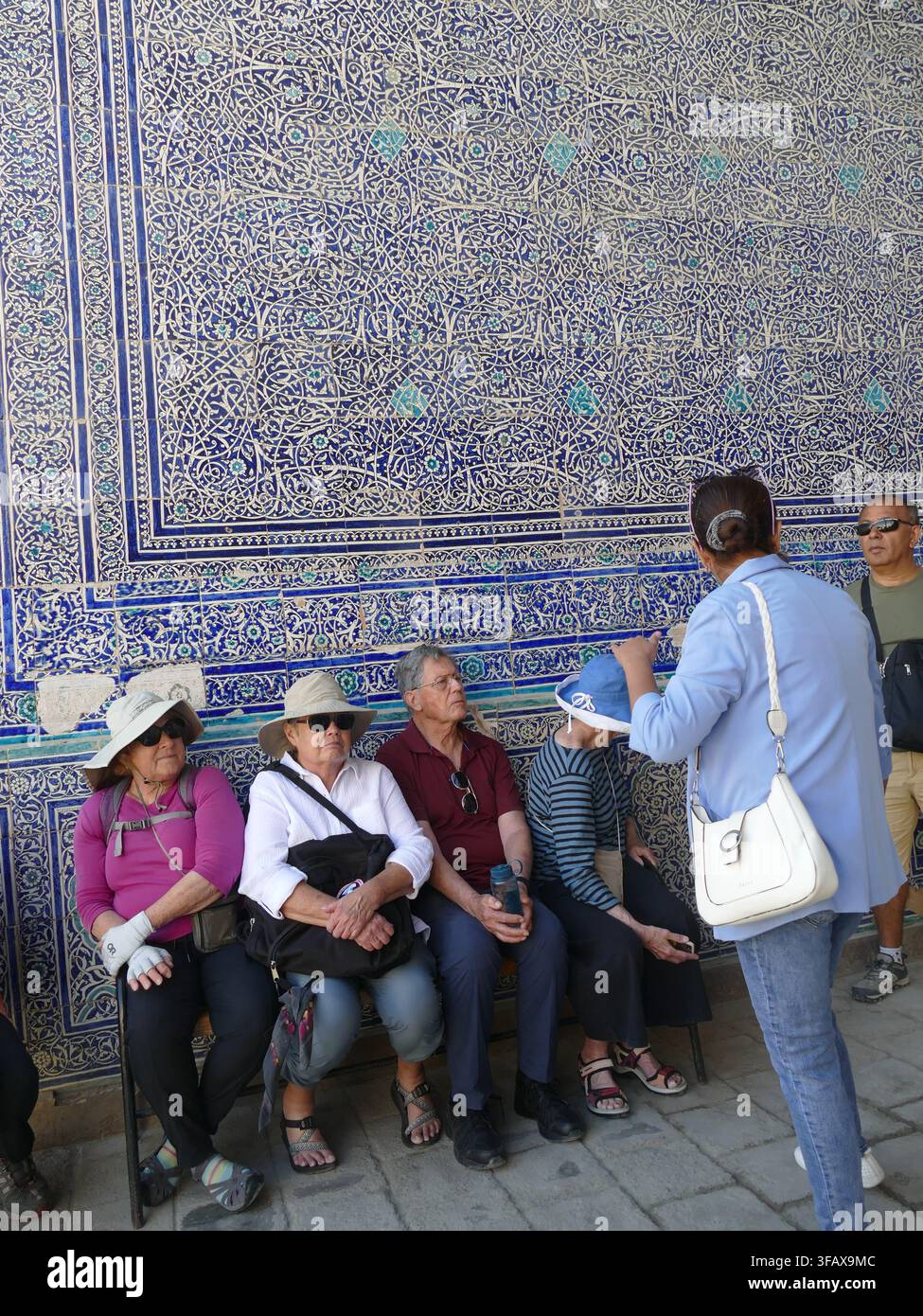 KHIVA, UZBEKISTAN - 14 SET 2024 - Turisti seduti e in ascolto di una guida turistica, che imparano sulla ricca cultura di Khiva e sulle intricate piastrelle islamiche uzbeke Foto Stock