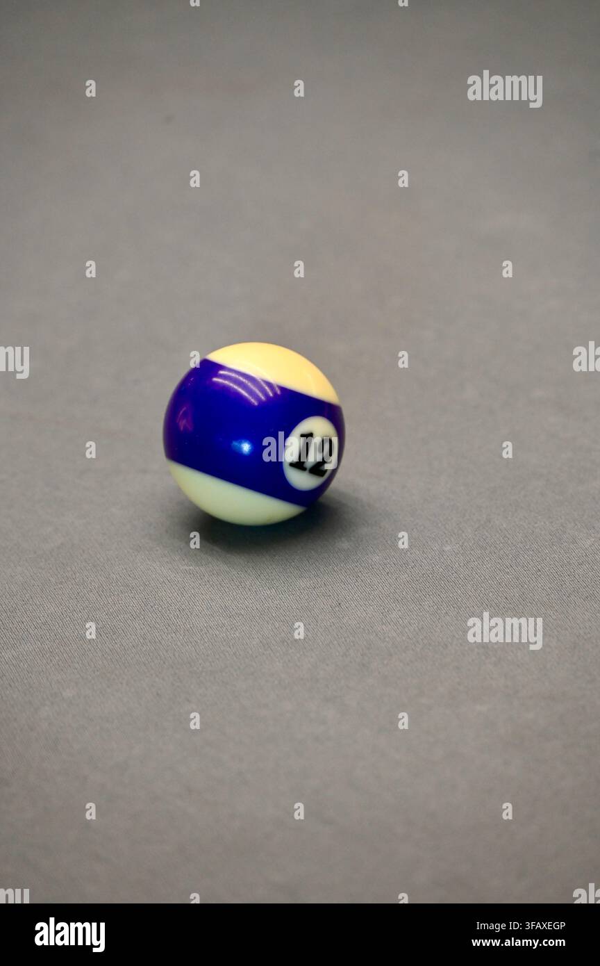 Una fotografia verticale in primo piano della palla da biliardo numero dodici a strisce viola e bianche, isolata su una moderna superficie di tavolo da biliardo in feltro grigio. Foto Stock