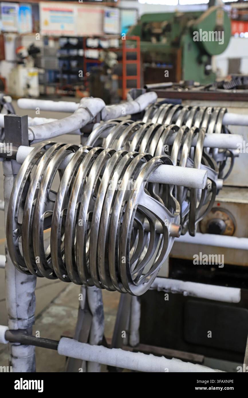In una officina industriale, due pile di semilavorati ad anelli metallici ordinatamente disposti sono fissate su pali, con attrezzature di lavorazione scure sullo sfondo Foto Stock