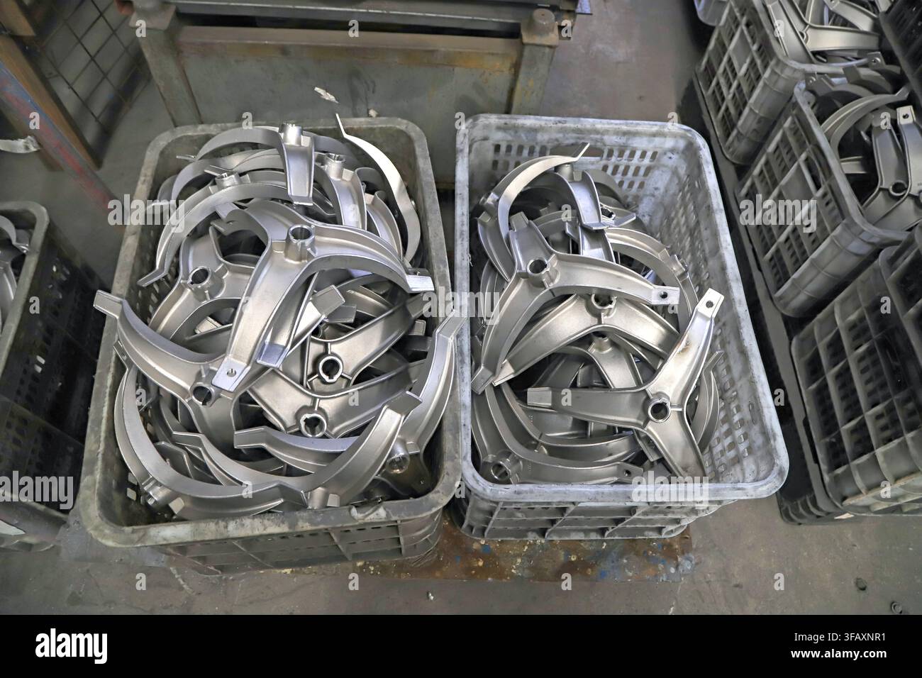 Due cassette di plastica piene di pezzi di fusione in metallo argentato a forma di stella a tre artigli, come componenti semilavorati nella produzione industriale, che mostrano pa Foto Stock