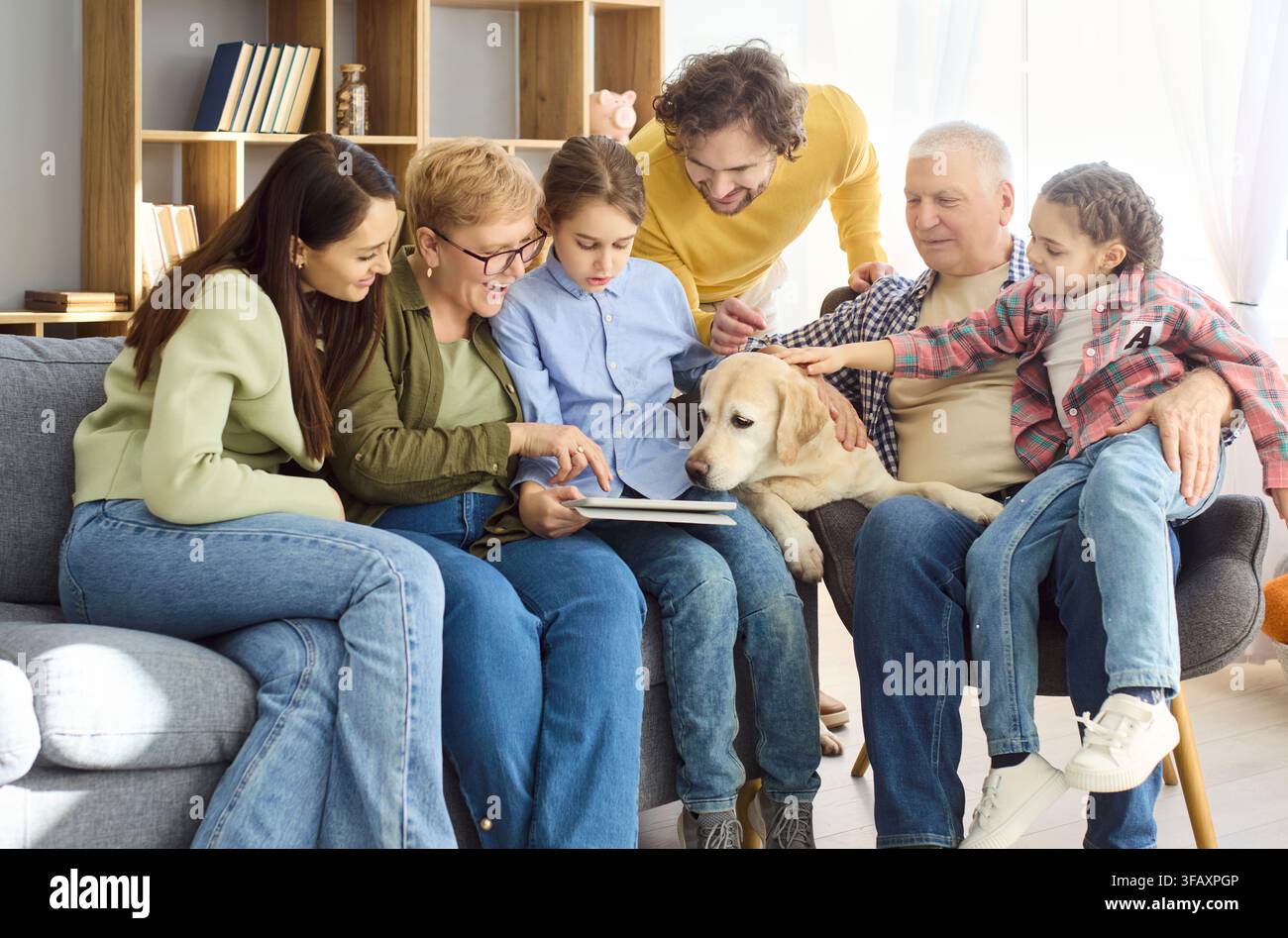 Nonni, genitori e bambini che usano insieme un tablet a casa con un cane sul divano Foto Stock