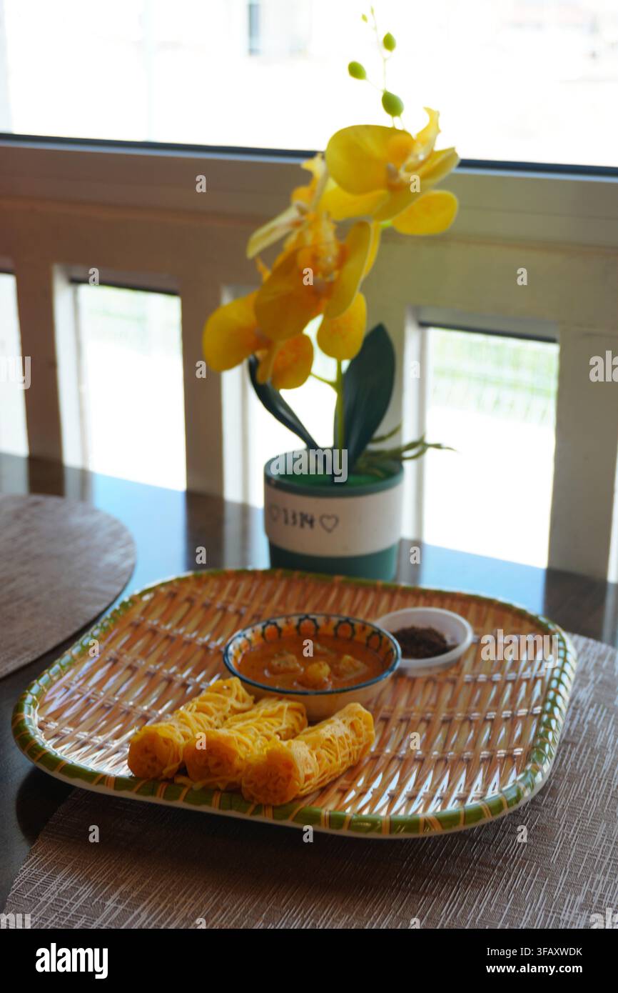 Set Roti Jala su tavolo da pranzo con decorazione di orchidea gialla, luce della finestra Foto Stock