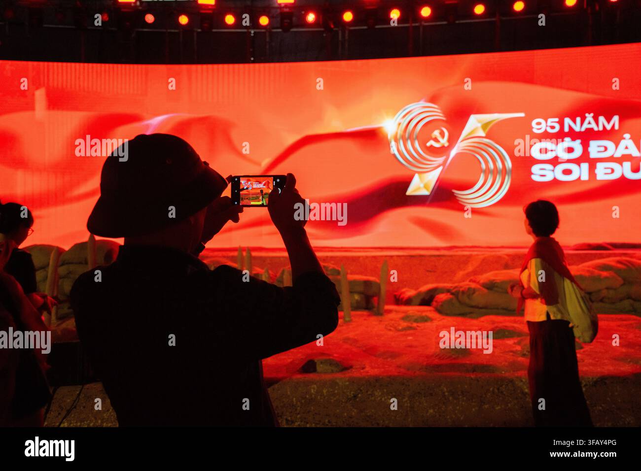 Visitatore che fotografa una mostra per l'anniversario del Partito Comunista di notte, Hanoi, Vietnam Foto Stock