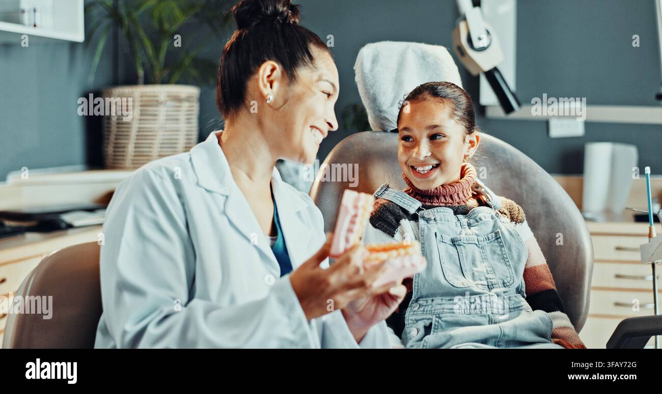 Dentista, donna e modello di dente con bambino, consulenza e appuntamento per il controllo. Assistenza sanitaria, spiegazione e consulenza con una bambina felice per l’odontoiatria Foto Stock