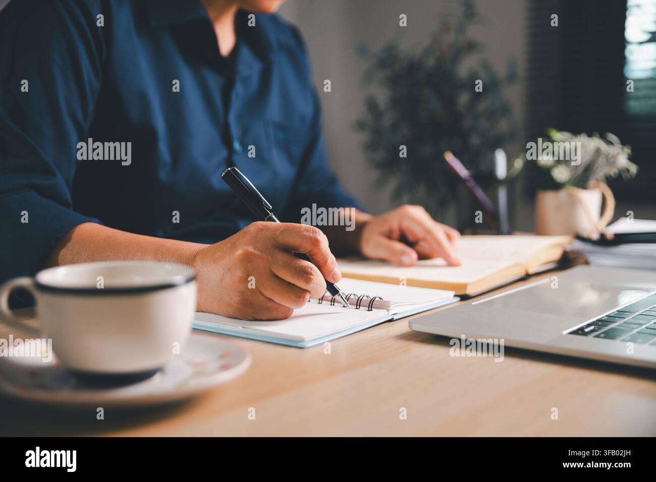 Appunti di studio professionali sulla scrittura mentre si legge un libro aperto accanto a un laptop e una tazza di caffè, rappresentanti ricerca accademica, istruzione online, preparazione agli esami Foto Stock