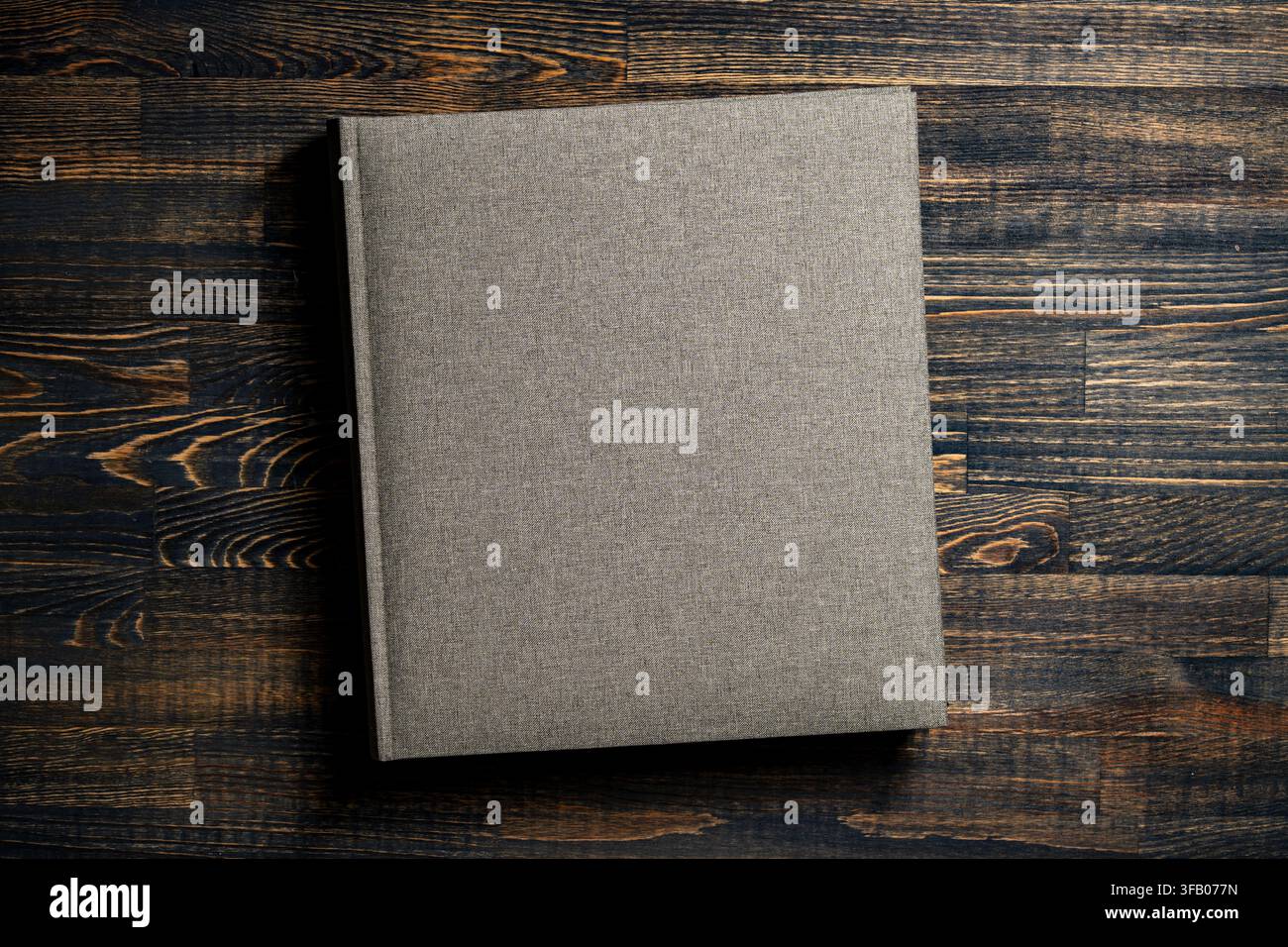 Modello di copertina di libro in lino vuota su sfondo di legno. Vista dall'alto di un album fotografico o libro in tessuto grigio con copertina rigida in lino su texture d Foto Stock