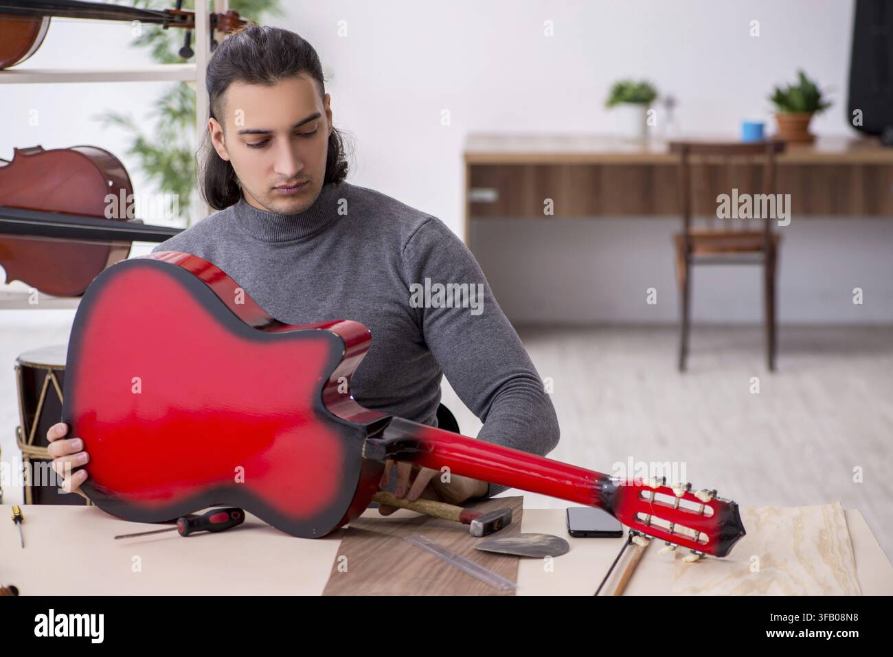 Giovane meccanico ripara una chitarra in officina Foto Stock