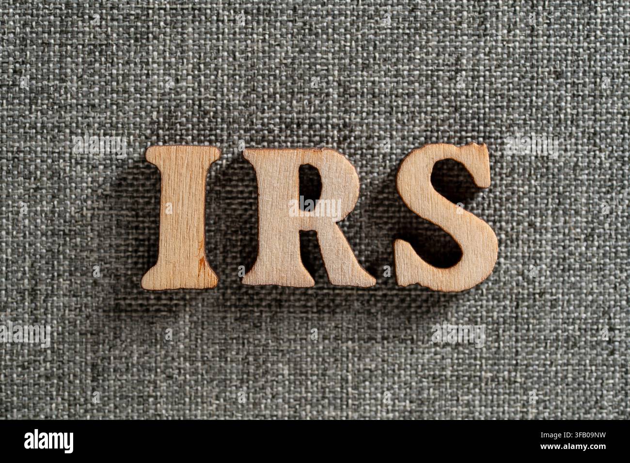 Parola IRS in lettere di legno su sfondo in tessuto grigio, primo piano. Abbreviazione IRS scritta con lettere di legno su superficie tessile grigia per le tasse, Foto Stock