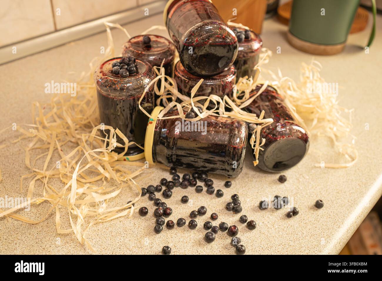 Barattoli di marmellata artigianale di mirtilli di bosco sparsi su un tavolo con bacche fresche e schegge di legno decorative, conserva biologica fatta in casa Foto Stock