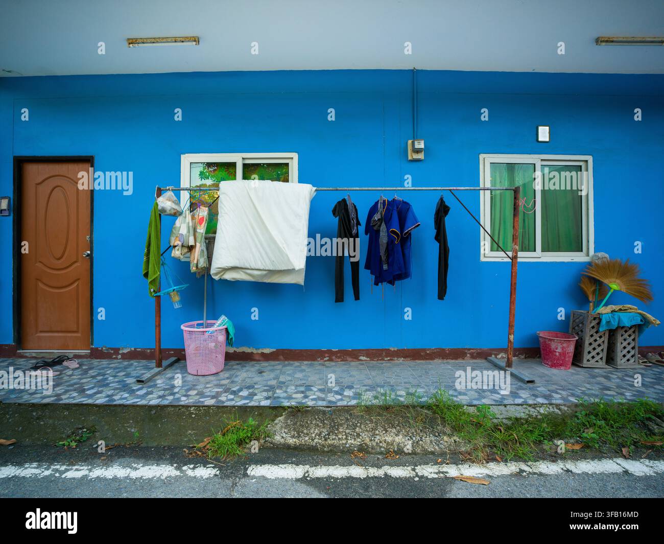 Abbigliamento, biancheria da letto e una muta subacquea appesi ad asciugare su una rastrelliera fuori da una casa residenziale dipinta di blu brillante a Kamala, Phuket, Thailandia. Foto Stock
