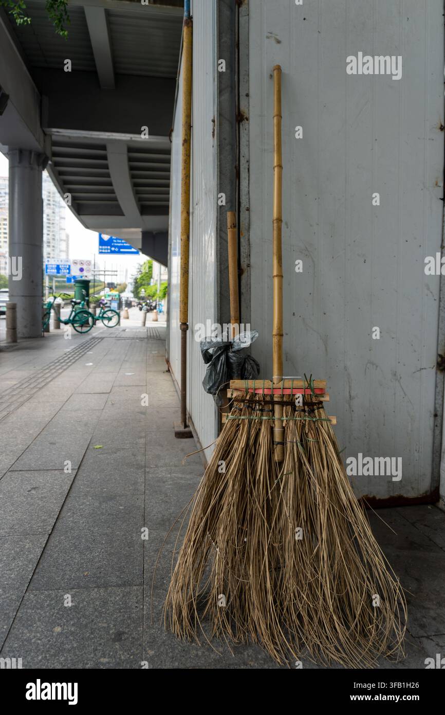 Scopa tradizionale di bambù appoggiata a un muro urbano. Foto Stock