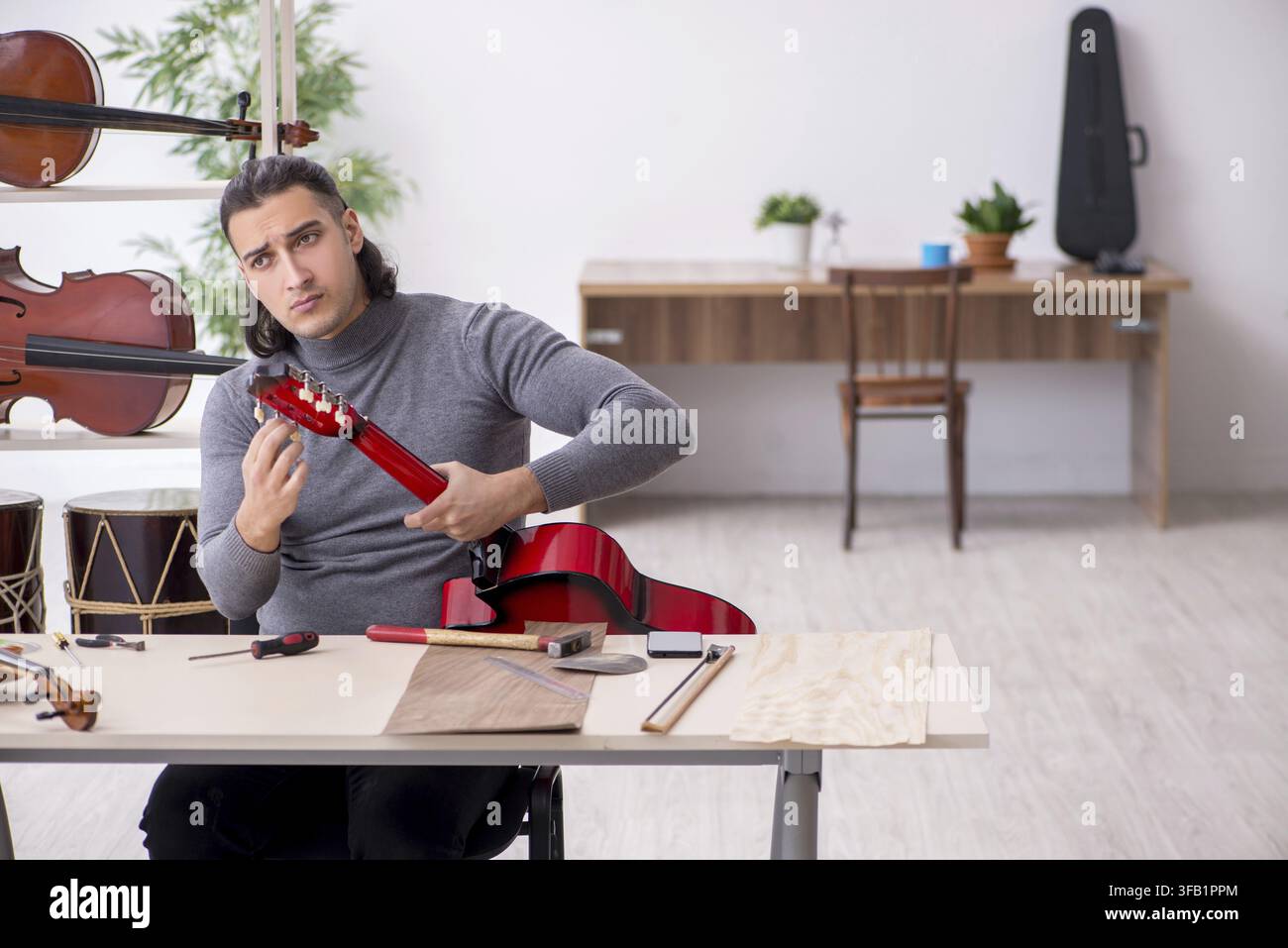 Giovane meccanico ripara una chitarra in officina Foto Stock