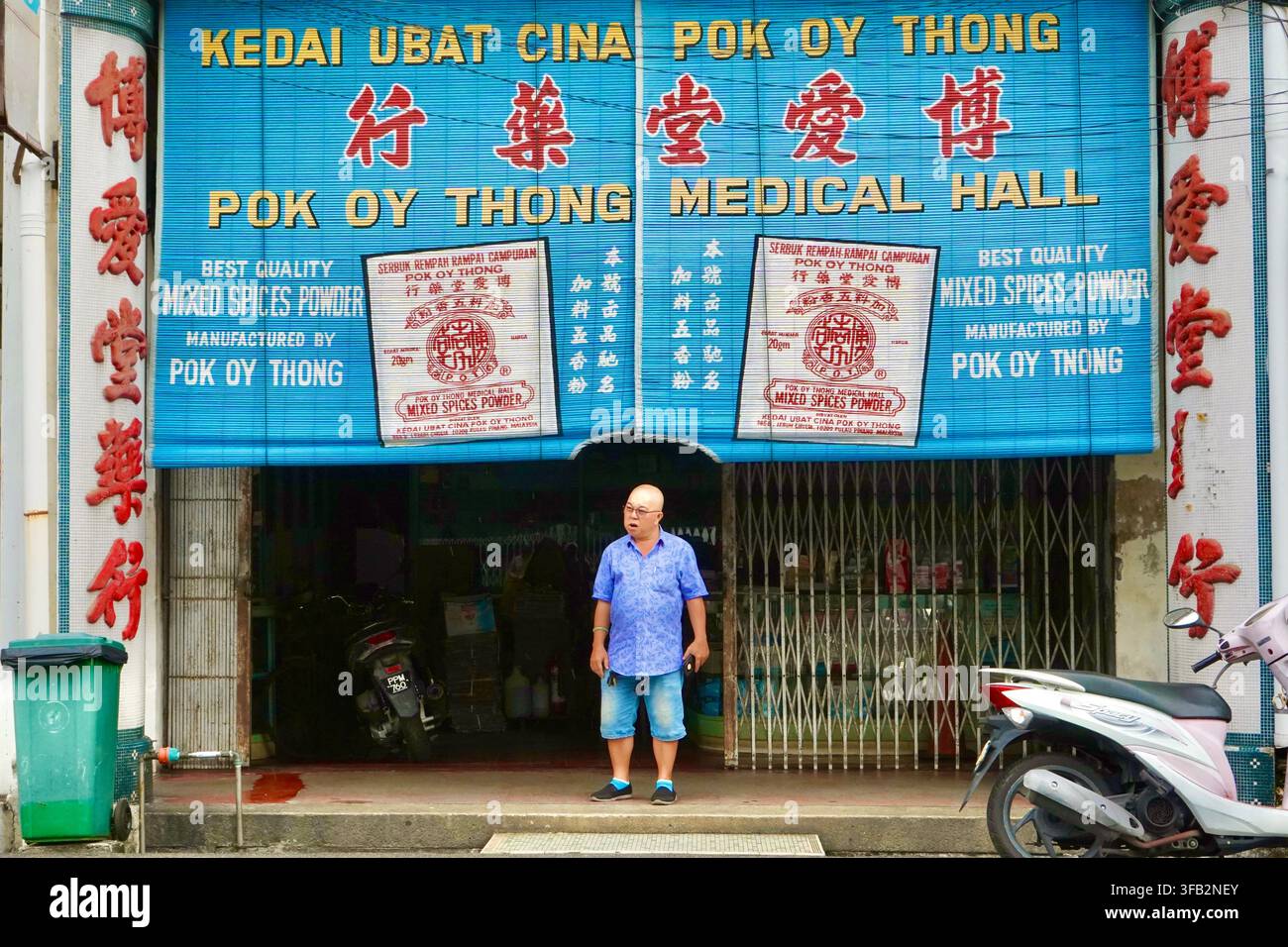 Uomo in piedi davanti alla vetrina della farmacia tradizionale cinese Pok Oy Thong Medical Hall con cartello blu a Penang, Malesia Foto Stock