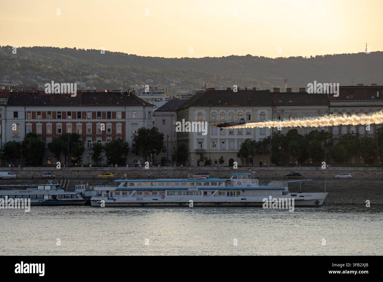 Budapest, Ungheria – 22 luglio 2026: Scatto teleobiettivo che cattura un aereo da acrobazia che esegue un passaggio a bassa quota con una lunga scia di fumo luminosa sopra la brughiera Foto Stock