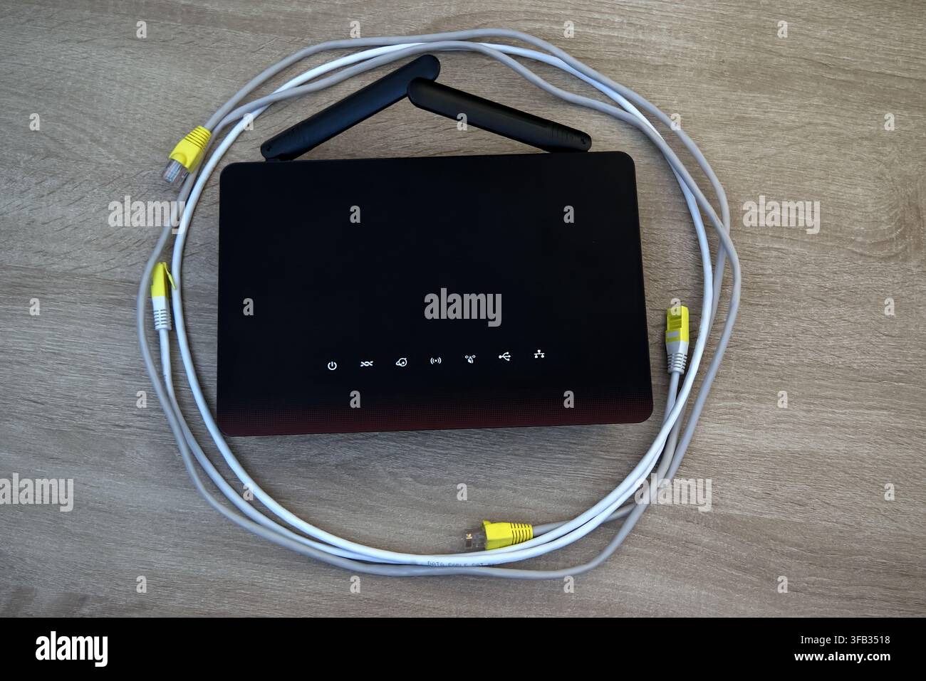 Fotografia flat lay di un router wireless al centro, circondato da cavi di rete bianchi e grigi ordinatamente arrotolati su uno sfondo di legno. Concetto di str Foto Stock