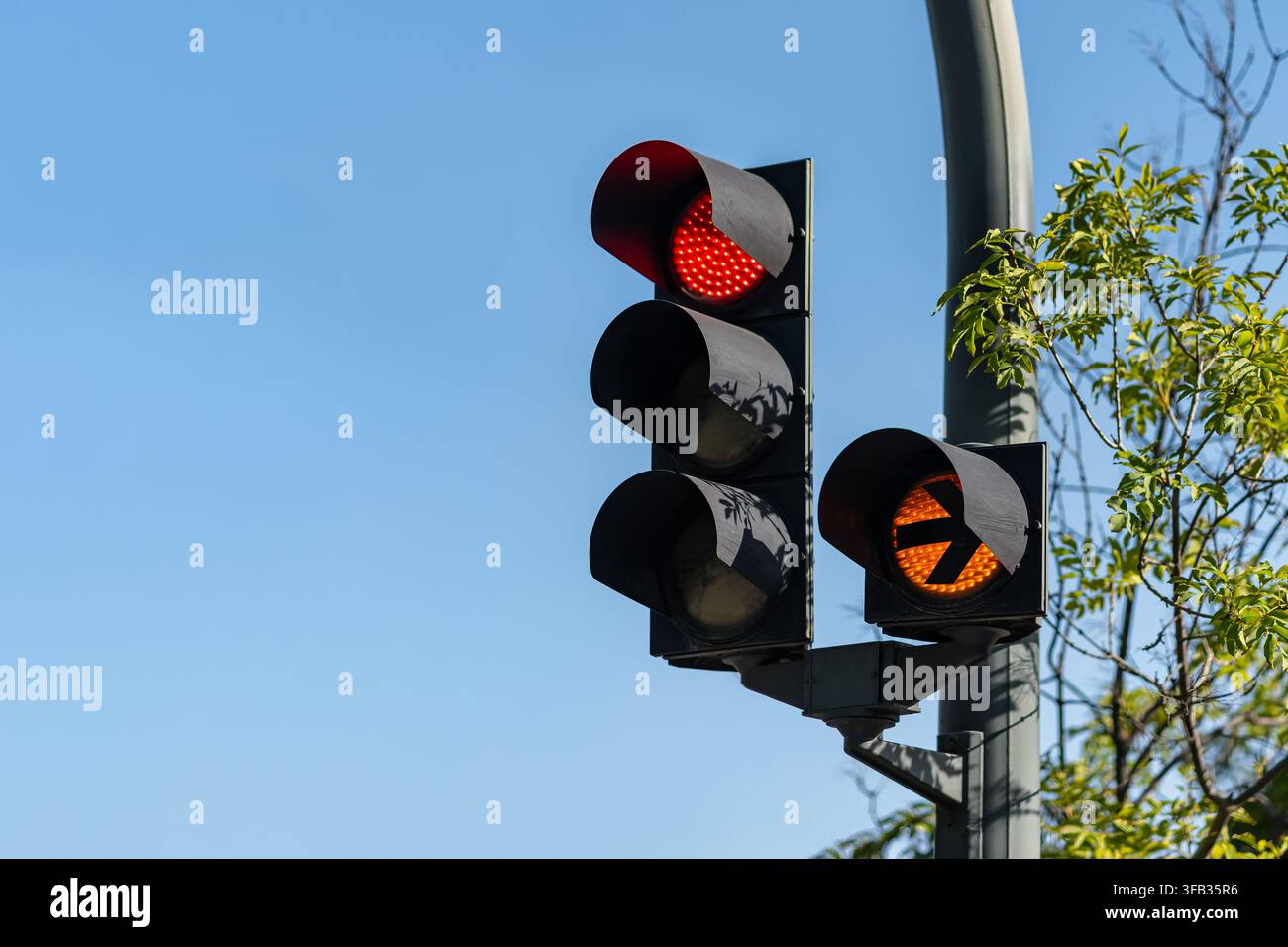 Semaforo rosso e freccia direzionale ambrata montati su un palo contro un cielo blu terso Foto Stock