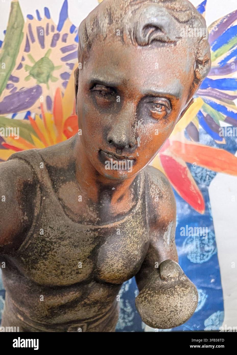 Un primo piano di una scultura di busto maschile in bronzo classico su uno sfondo di opera artistica floreale vivace e multicolore. Foto Stock