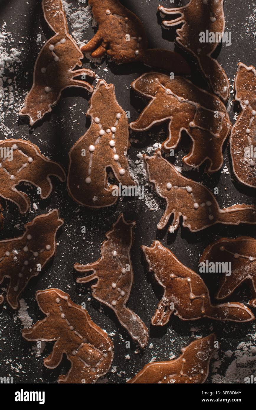 Vari biscotti di pan di zenzero a forma di animali del bosco, decorati con glassa bianca e spolverati di zucchero a velo su una superficie rustica scura per la cottura. Foto Stock