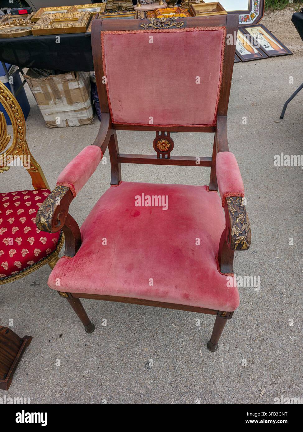 Una poltrona vintage in legno scuro con braccioli intagliati e rivestita in velluto rosa polveroso è mostrata all'aperto in un mercato. Il tessuto sembra consumato Foto Stock