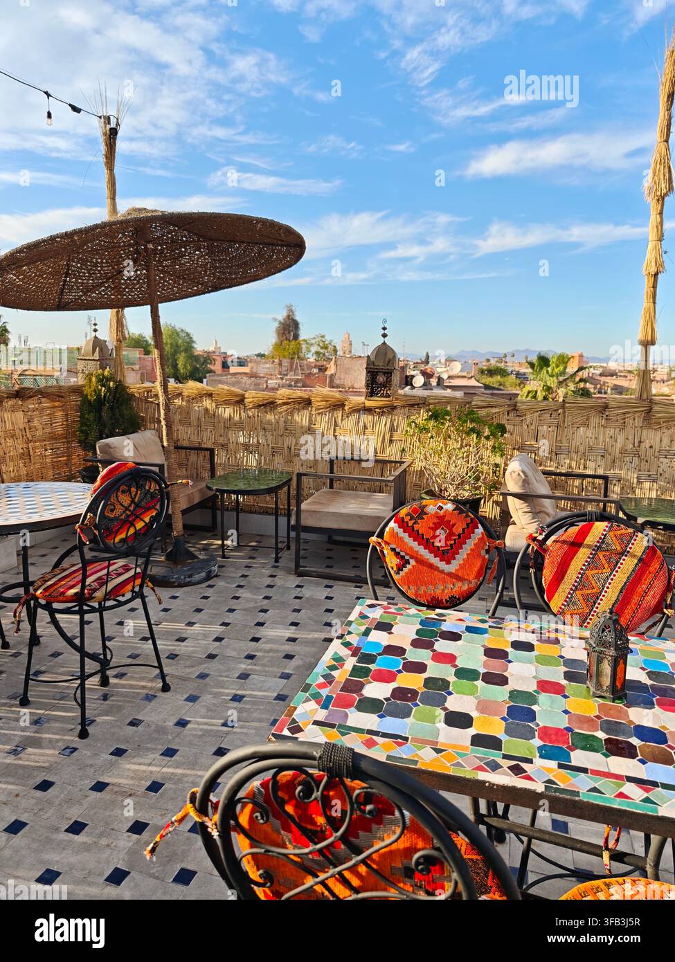 Colorata terrazza marocchina sul tetto a Marrakesh con tavoli a mosaico, sedie tradizionali e vedute panoramiche della città. Foto Stock