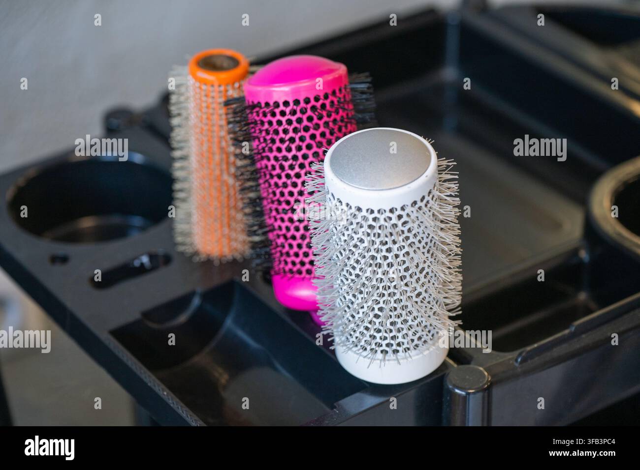 Un primo piano di tre spazzole per capelli rotonde in ceramica colorate organizzate in un vassoio di carrello da salone in plastica nera. Foto Stock