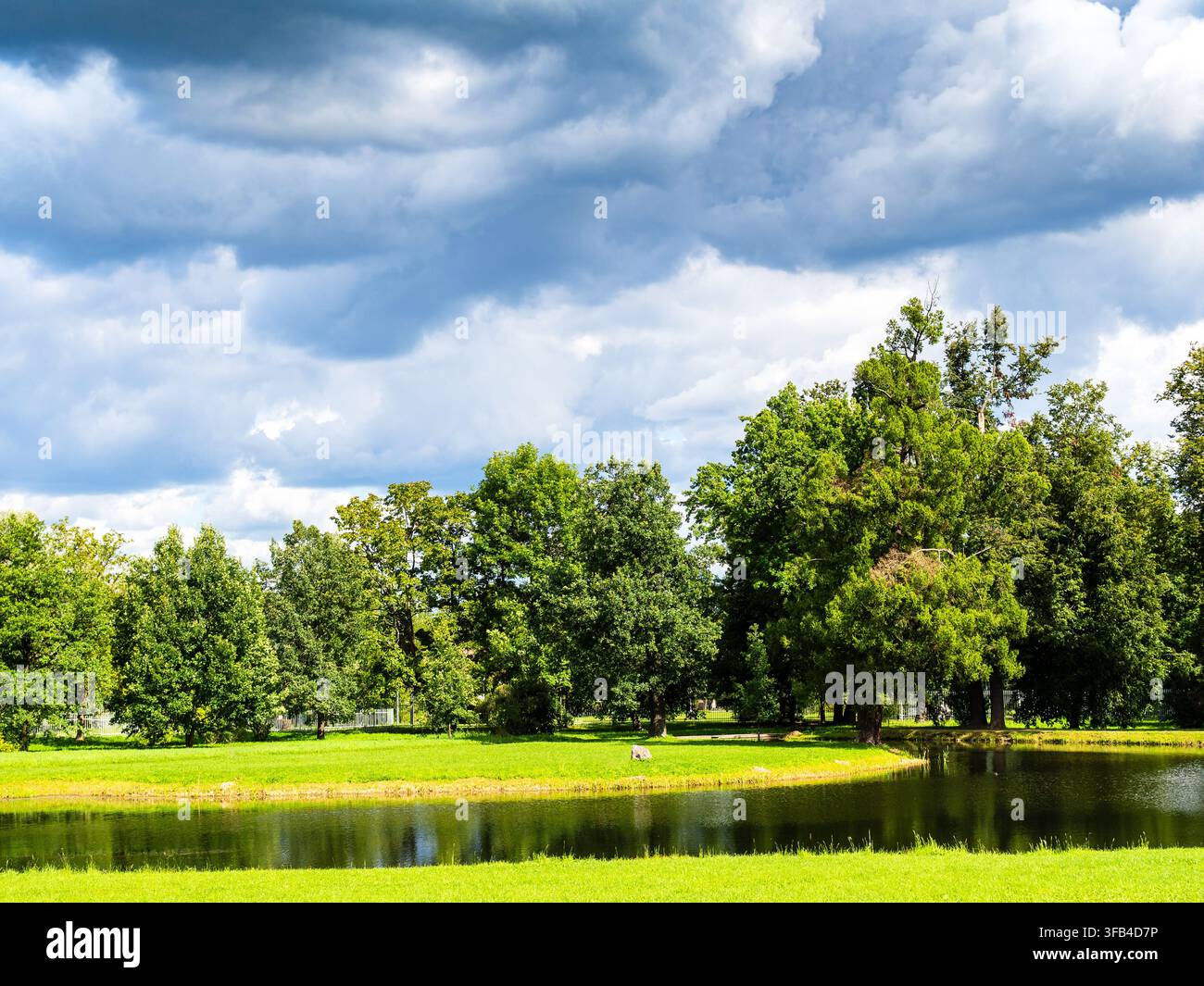 nuvole blu scuro piovose sopra un boschetto verde e uno stagno nel parco Aleksandrovsky nella città di Tsarskoye Selo in una giornata estiva soleggiata Foto Stock