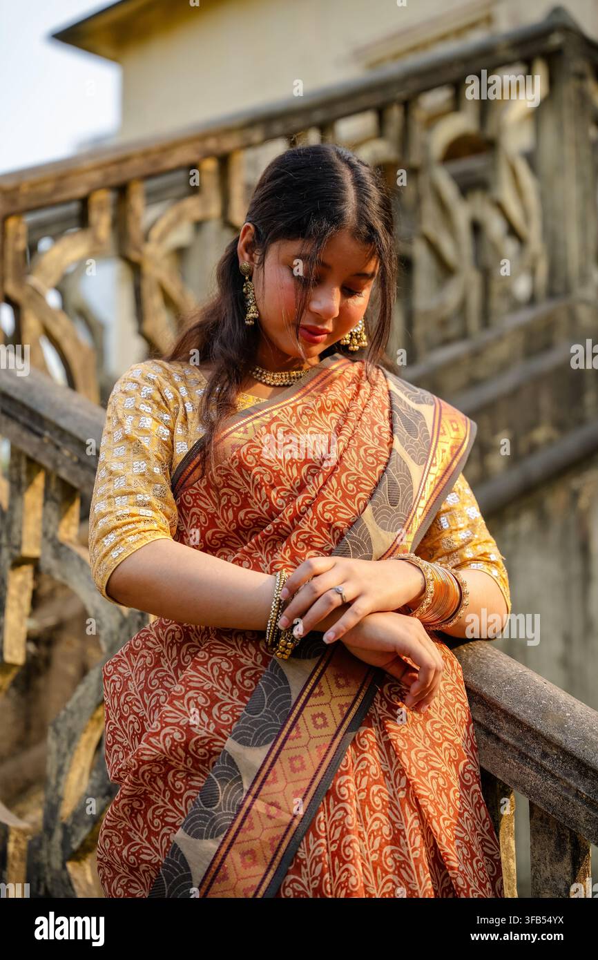 Una donna in un tradizionale saree è in piedi su un ponte di legno con ringhiere intricate, tenendo un ventaglio decorativo. Foto Stock