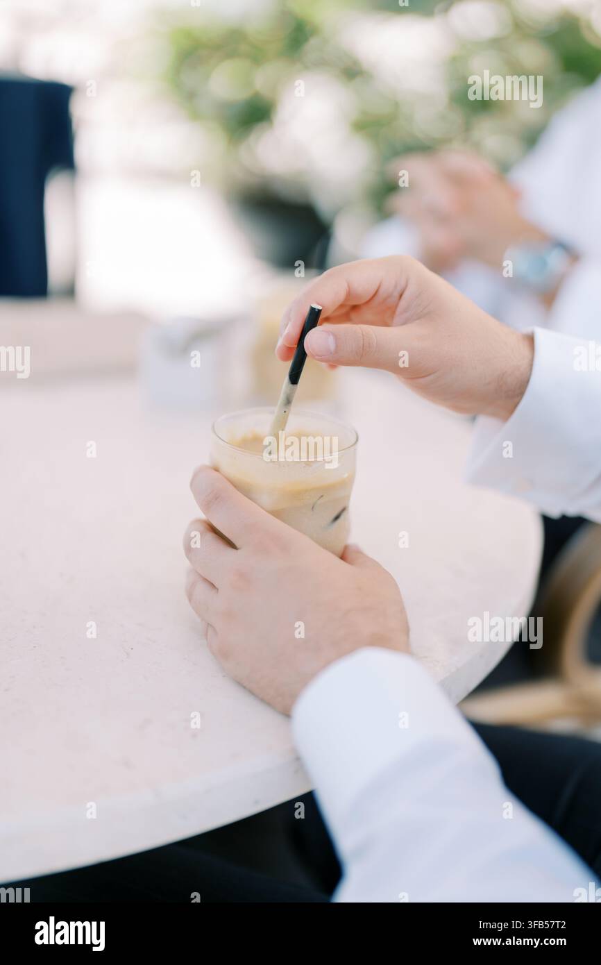 Prima vista di una mano che mescola caffè freddo a un tavolo da caffè Foto Stock