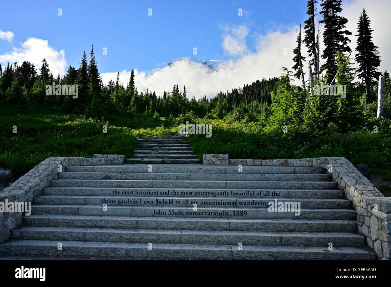 Scalini di pietra incisi con una citazione di John Muir che conducono a un sentiero montano panoramico con il Monte Rainier che si erge sopra le nuvole, Stato di Washington, USA. Foto Stock
