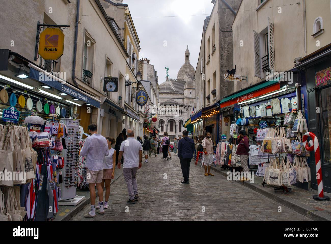 I negozi di souvenir costeggiano una strada acciottolata di Montmartre con la cupola della Basilica del Sacro Cuore visibile sopra gli edifici, Parigi, Francia. Foto Stock