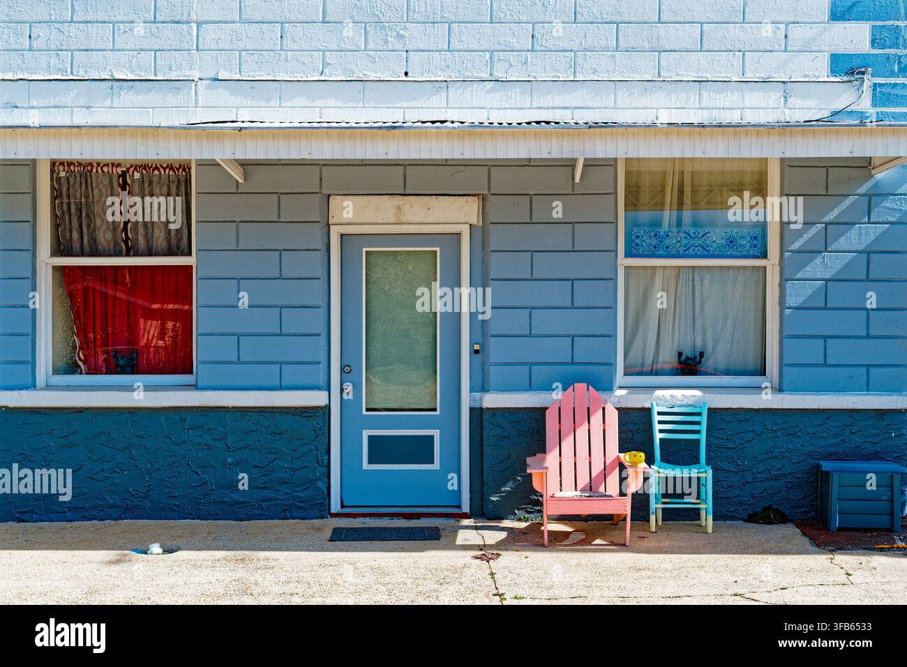 Casa in blocchi di cemento blu con finestre e porta d'ingresso con una sedia Adirondack rosa e una sedia dritta blu sul portico. Wetumpka Alabama Foto Stock