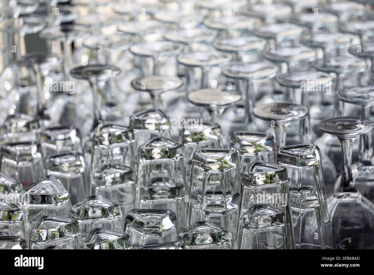 Le stoviglie di vetro trasparenti sono disposte a testa in giù in file organizzate. Calici e bicchieri misti formano un layout denso. Le stoviglie sono pronte per il servizio. Foto Stock