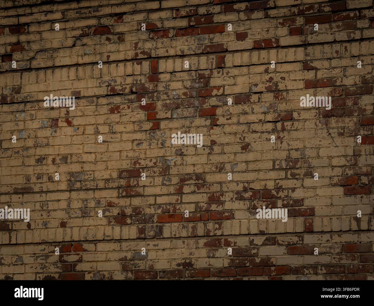 Una texture di muro di mattoni consumata e invecchiata con vernice beige e marrone chiaro che si stacca, mostrando i mattoni rossi sottostanti in un design urbano Foto Stock