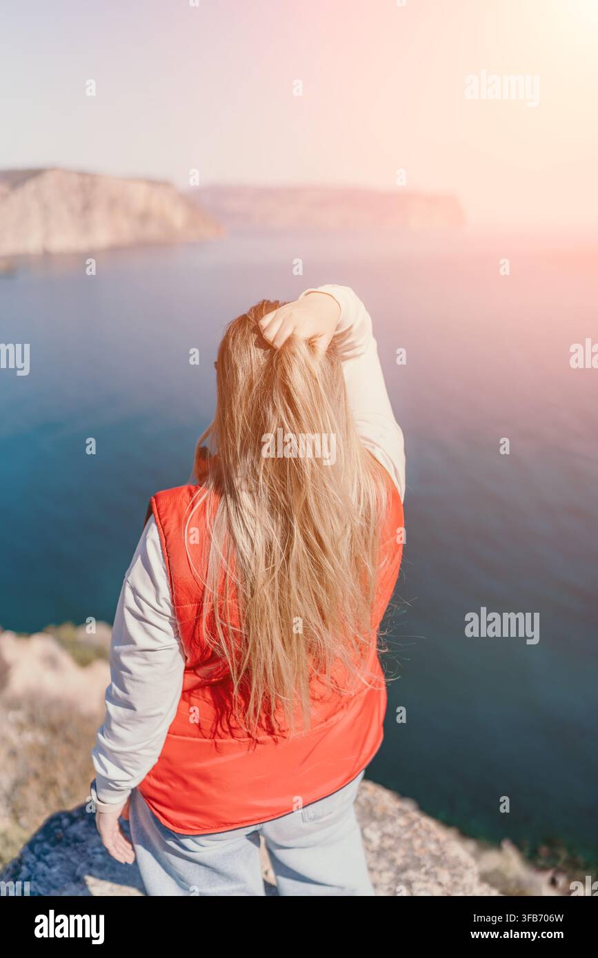 Donna su una scogliera sul mare in piedi su un bordo roccioso che guarda l'oceano blu durante un tramonto luminoso con spazio per il testo Foto Stock