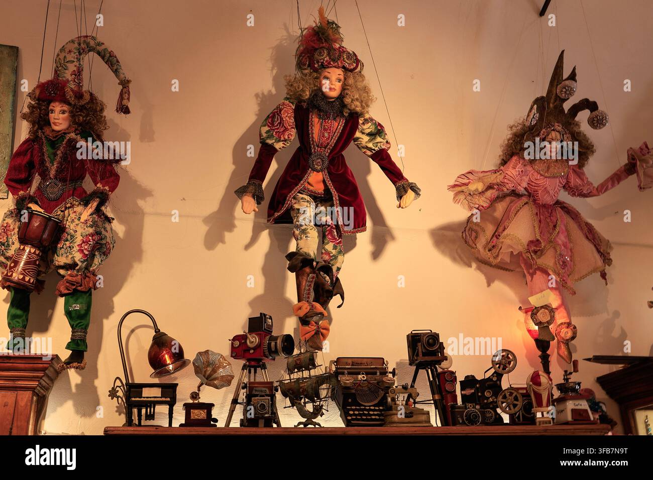 Oia, Santorini, Grecia – 4 agosto 2026: Tre marionette ornate fatte a mano sono appese sopra una mensola di macchine fotografiche antiche e oggetti da collezione in un negozio Foto Stock