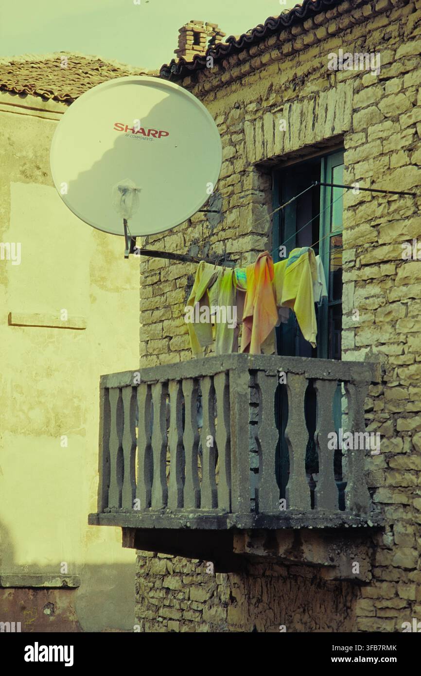 Vecchio balcone di legno su casa in pietra con antenna satellitare e biancheria colorata ad asciugare. Tepelenë, distretto di Gjirokastër, Albania, Europa Foto Stock