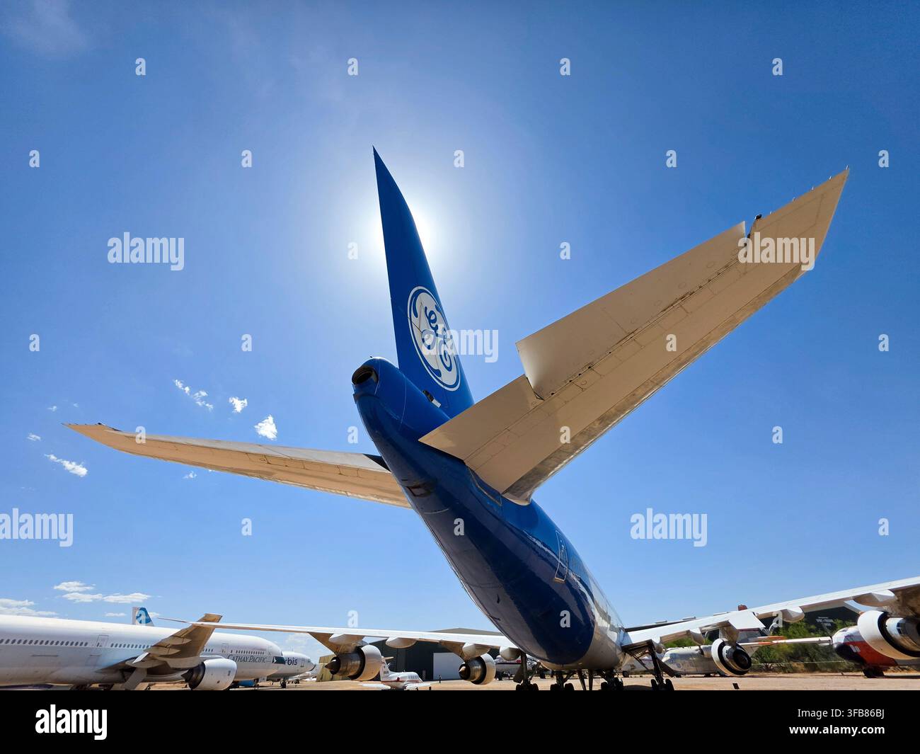 Ala di coda blu con logo GE General Electric contro il sole luminoso; aereo GE visto da dietro - Immagine stock catturata con smartphone