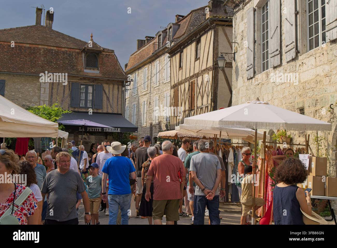 Mercato domenicale affollato nel villaggio medievale di Issigeac, Dordogna, Francia, con case a graticcio, bancarelle e posti a sedere al ristorante all'aperto. Foto Stock