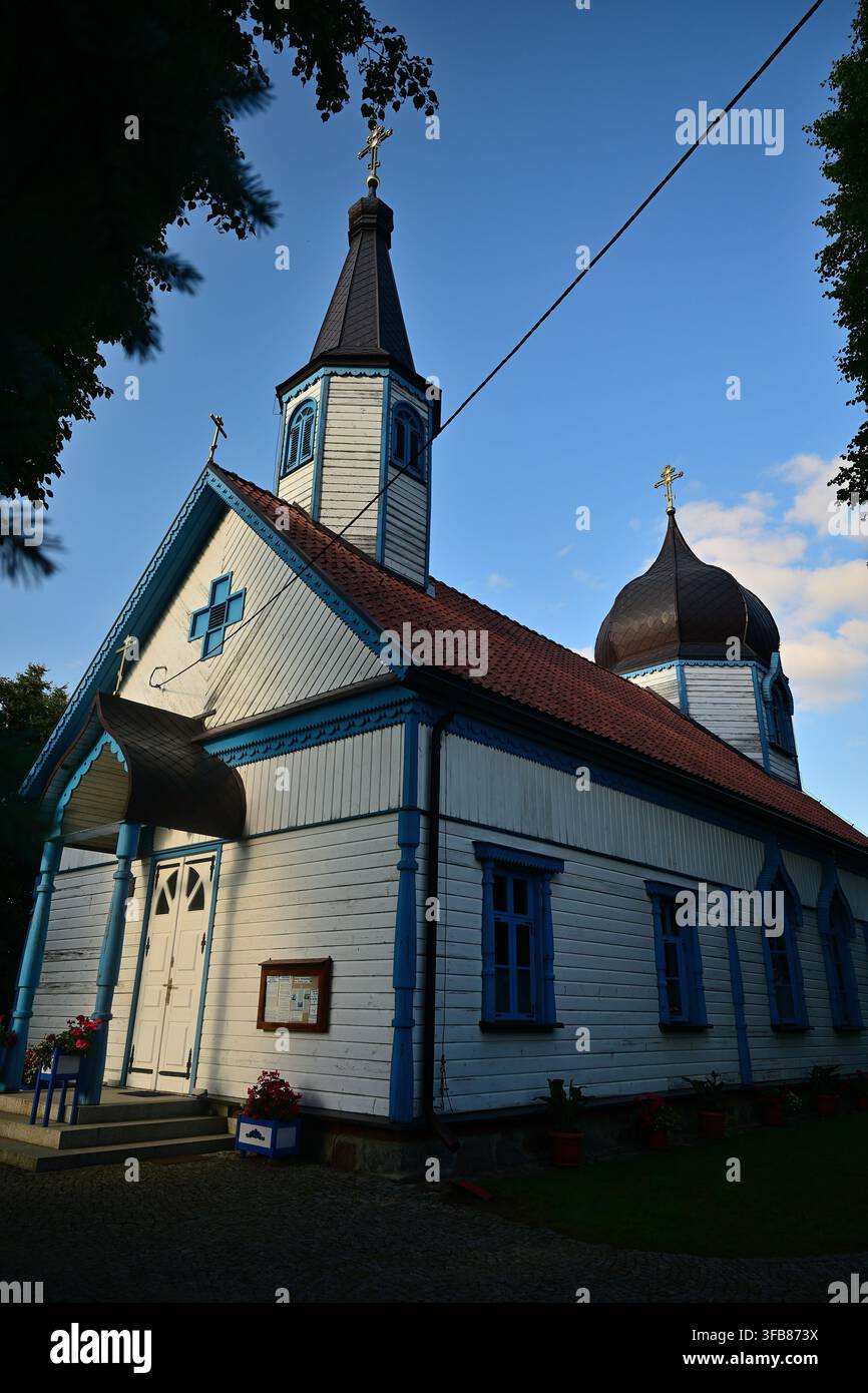 Chiesa ortodossa in legno bianco e blu con una cupola a cipolla e una torre in un villaggio rurale al tramonto - Chiesa ortodossa a Wojnowo. Foto Stock