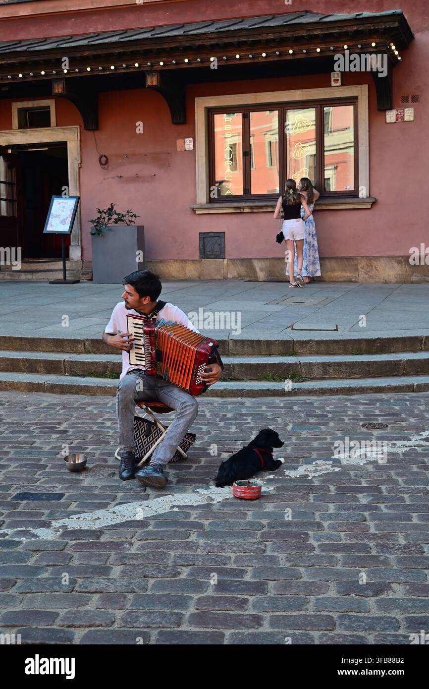 Musicista di strada che suona l'accordione su una piazza lastricata con un cane e turisti nelle vicinanze a Varsavia, Polonia. Foto Stock