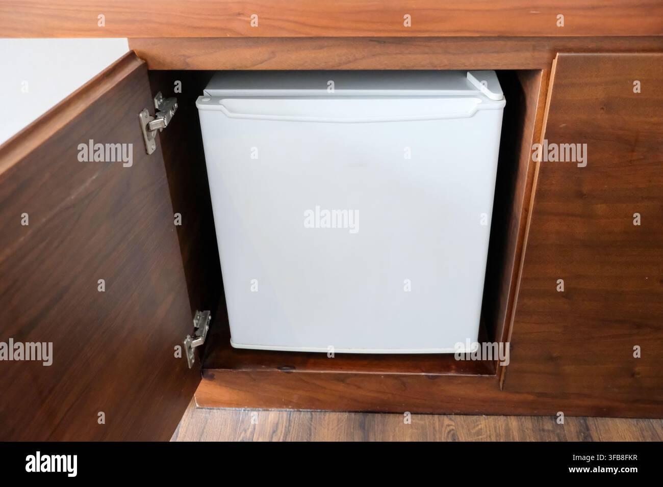 Mini-frigo bianco compatto integrato in mobili su misura in legno scuro Foto Stock