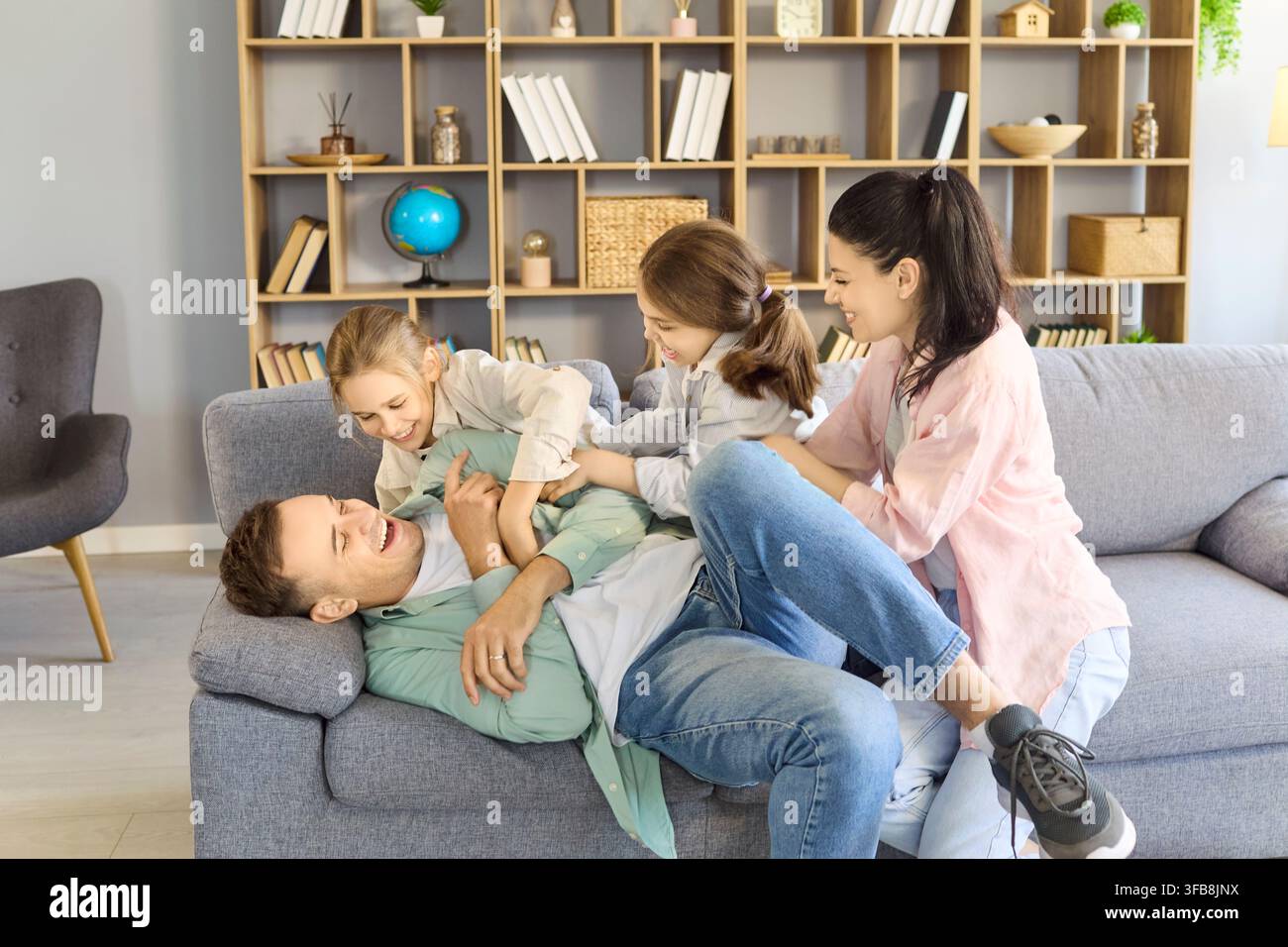 Genitori e bambini giocosi che si fanno il solletico a casa sul divano, divertimento familiare allegro Foto Stock